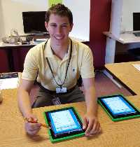 Aaron smiling sitting at a desk with a tablet. 